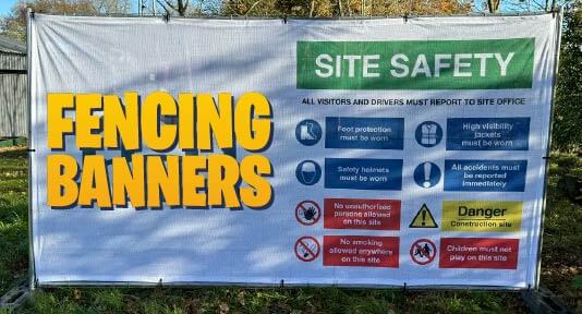 showing a construction site barrier with a mesh banner/sign installed on it